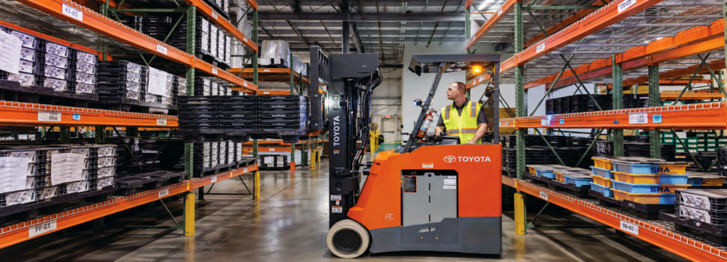 Toyota Stand-Up Rider forklift operating in a narrow warehouse aisle