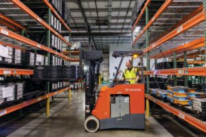 Toyota Stand-Up Rider forklift operating in a narrow warehouse aisle